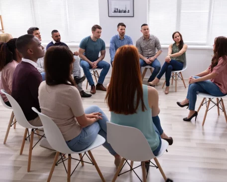 A small group of people seated in a circle, engaging in a supportive discussion during a therapy session in Dorset.